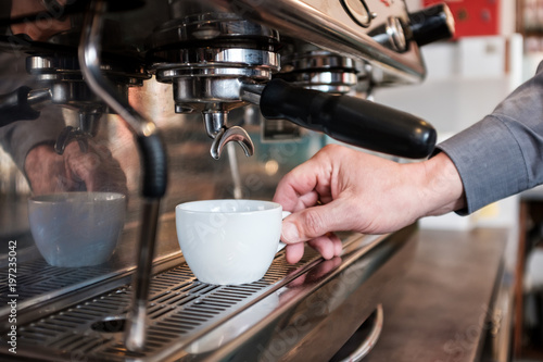Barista placing cup in coffee machine to making fresh espresso