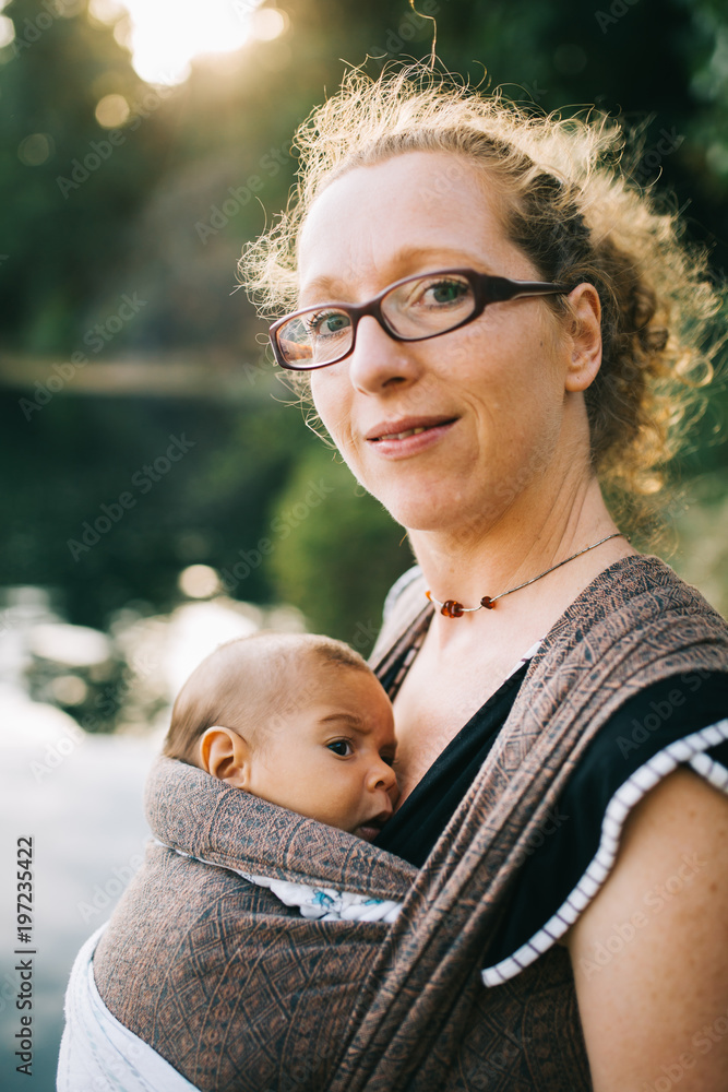 Obraz premium Blonde caucasian mom holding her colored child in a sling