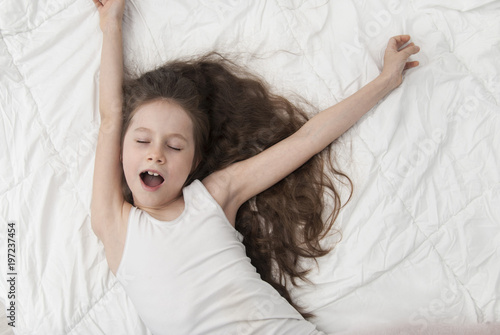 Cute Smiling Little Girl Woke up in White Bed. Morning in Wekeend. Flat Lay. Girl who Spreads in the Morning after Sleep Sleeping children Concept photo