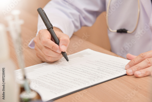 Asian male doctor is writing something on clipboard.