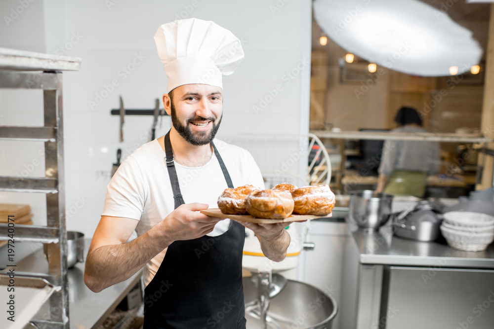 Portrait of a handsome confectioner stnading with sweet pastry in the professional kitchen Portrait of a handsome confectioner stnading with sweet pastry in the professional kitchen