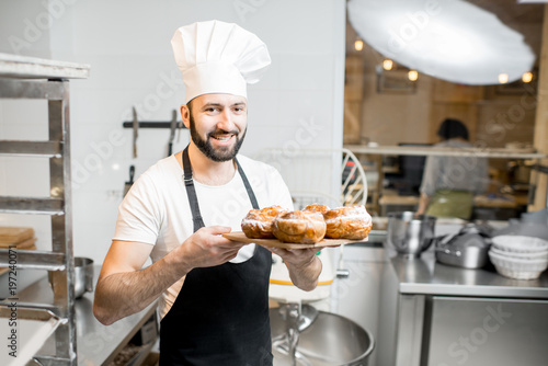 Portrait of a handsome confectioner stnading with sweet pastry in the professional kitchen