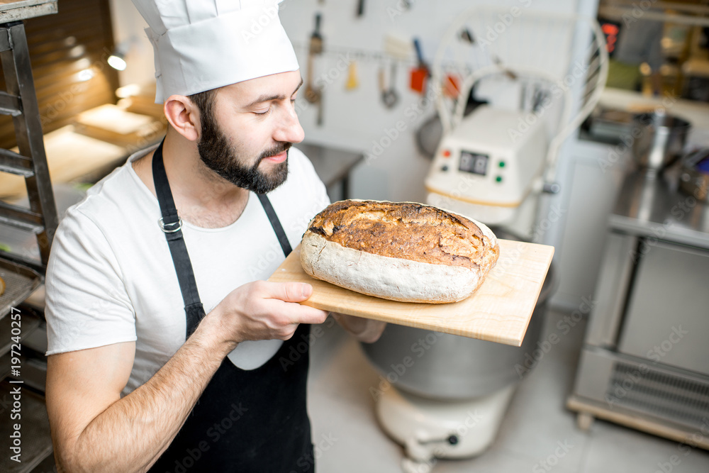 Portrait of a handsome baker in uniform standing with fresh bread in the small bakery manufacturing Portrait of a handsome baker in uniform standing with fresh bread in the small bakery manufacturing