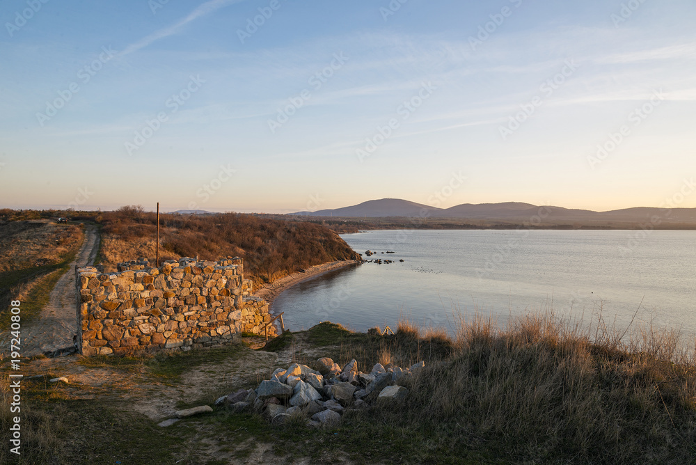 Fototapeta premium The tower of an ancient fortress on the beach. Winding coastline. Sunset.