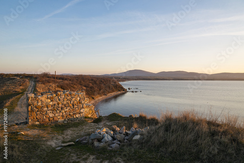 The tower of an ancient fortress on the beach. Winding coastline. Sunset.
