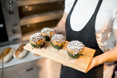 Confectioner holding delicious maffins on the professional oven background in the bakery photo