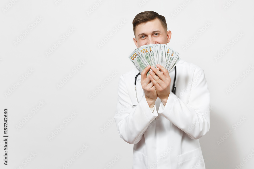 Smiling young doctor man isolated on white background. Male doctor in medical uniform, stethoscope holding bundle of dollars, banknotes, cash money. Healthcare personnel, health, medicine concept. Smiling young doctor man isolated on white background. Male doctor in medical uniform, stethoscope holding bundle of dollars, banknotes, cash money. Healthcare personnel, health, medicine concept.