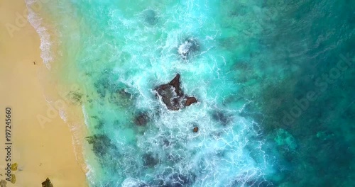 Overhead Pan Of Waves Breaking On Sandy Tropical Shore With Submegred Rocks - Bali, Indonesia photo