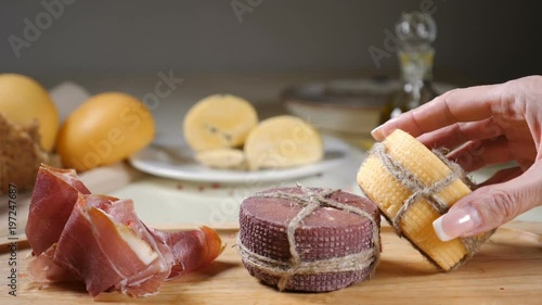 Restaurant concept. Table setting. Different pieces of cheeese decorated with rope are on wooden background with home made bread, nuts and olive bottles. Female hand takes away one piece . Slow motion photo