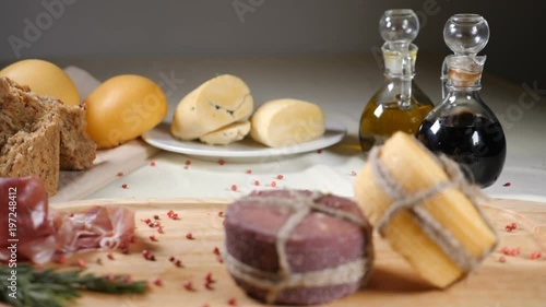 Restaurant concept. Table setting. Two pieces of cheeese decorated with rope are on wooden background with home made bread, nuts and olive bottles. Nuts and pepper fall down. Slow motion. photo