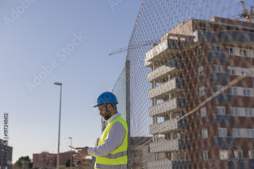 Architect or Engineer using tablet on the Construction Site. Daytime. Wearing protection equipment