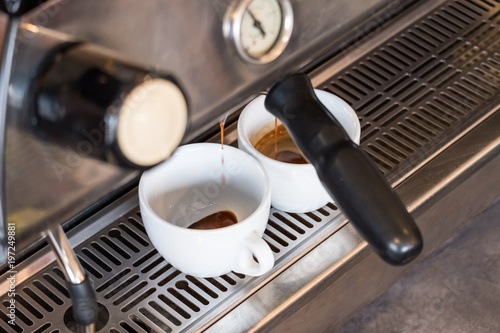 Espresso dripping from portafilter of coffee machine into white cup