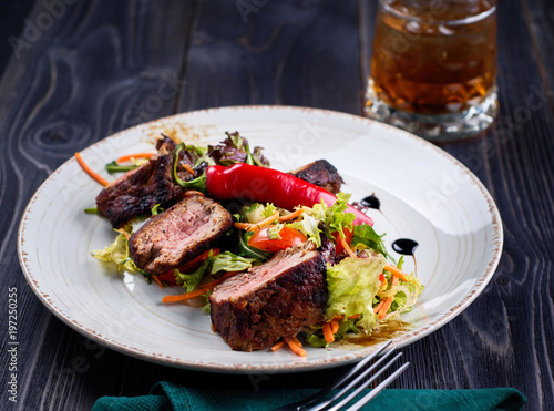 Veal salad with lettuce, carrot, tomato and pepper on white plate on dark wooden background, copy space. Restaurant food, close up. Meat salad and glass of whiskey