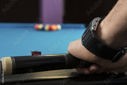 A close up of a hand holding a billiard cue and in the background a rack of 8 ball.
