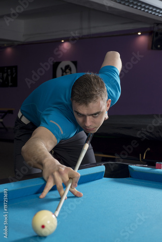 Close up view of a pool player performing a shot on a ball with chalk on the side of the table.