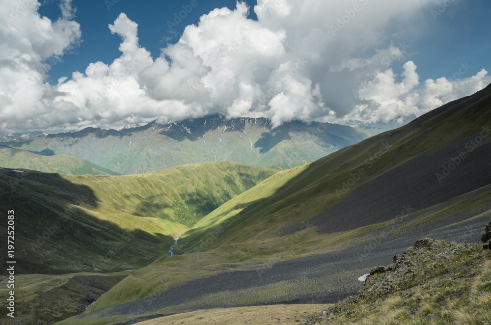 Summer day in Caucasus mountains at Tusheti, Georgia. Hills on the foreground. Mountain range and white clouds above it on the background. Concept of clear ecosystem.