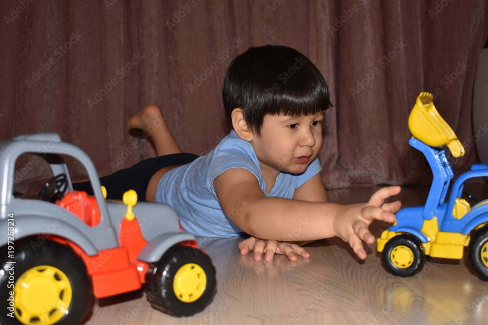 Little brown-eyed brunette boy in blue t-shirt plays on the floor with cars, tractor and bulldozer toys Little brown-eyed brunette boy in blue t-shirt plays on the floor with cars, tractor and bulldozer toys