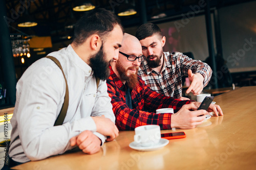 Friends of a man rest in a cafe   looking in the phone and discussing what they see