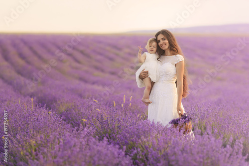 Happy beautiful mother and cute little daughter have fun in aroma lavender fields. Family holiday in summer day.