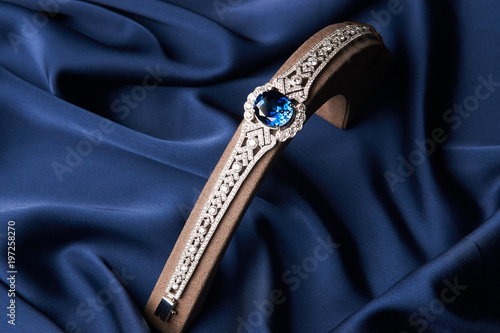 Beautiful platinum bracelet. Luxury women bracelet with diamonds and sapphire on blue silk background, close-up