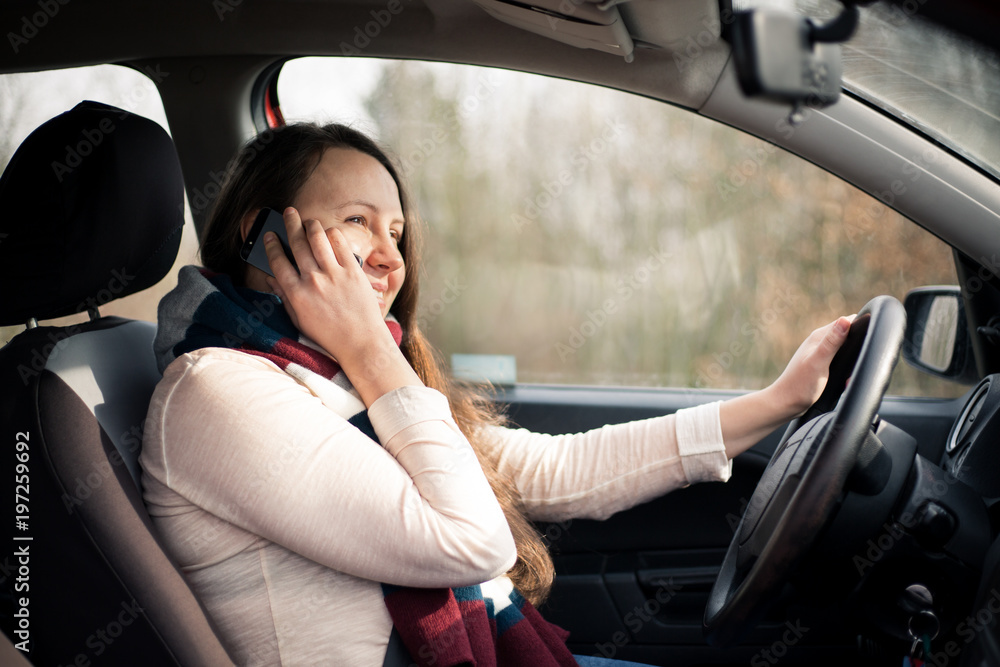 Pretty young brunette woman calling during driving car, using smartphone in the car