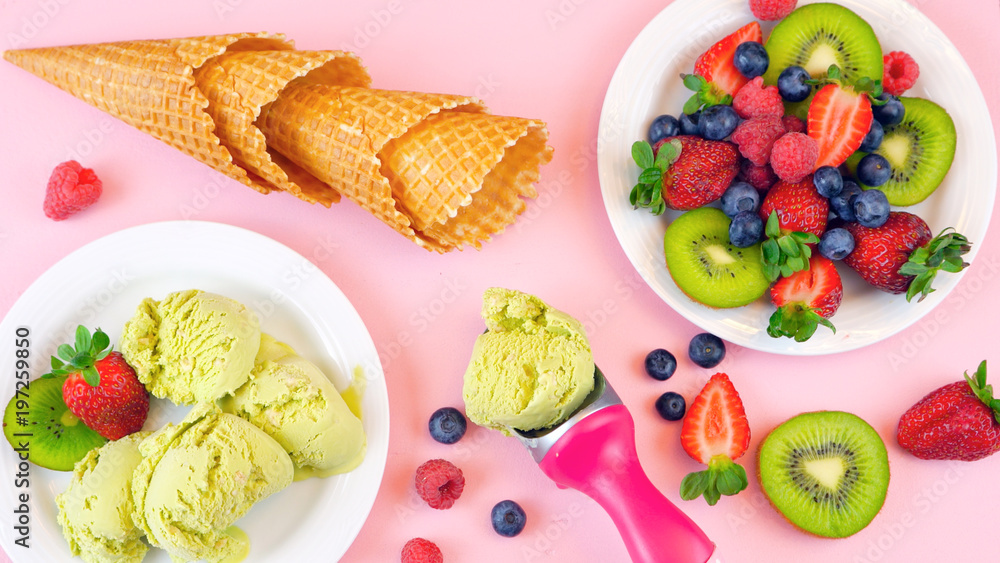 Serving Matcha Green Tea ice cream with waffle cones and fresh fruit on pink wood table, overhead flat lay.