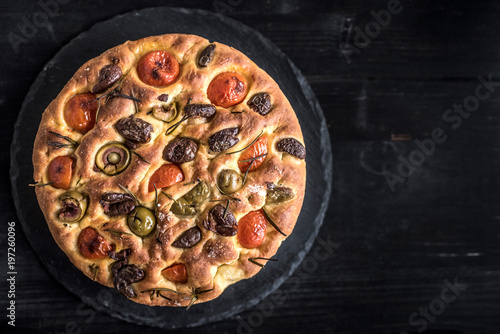 Homemade Italian Focaccia bread with olives and tomatoes on dark background with blank space