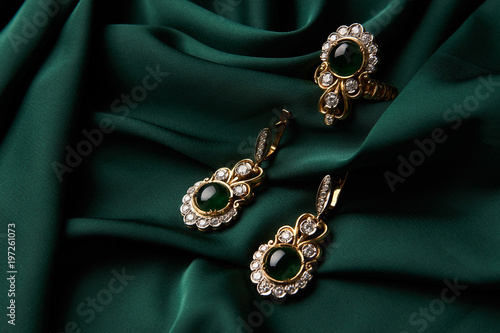 Diamond ring and earrings with emerald on a green silk background. Luxury female jewelry, close-up