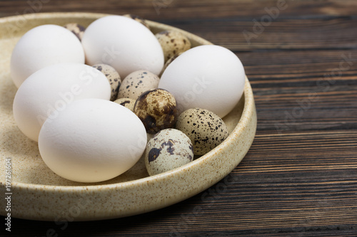 Easter concept. White chicken eggs and quail eggs on wood background on a plate close up. Minimal concept. Design, visual art.