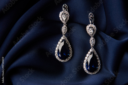 Pair of platinum earring with sapphire on blue satin background. Luxury female jewelry, close-up