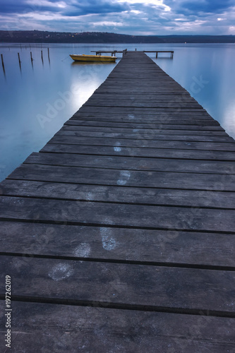 Tracks of steps on wooden pier and fishing boat at the lake after sunset
