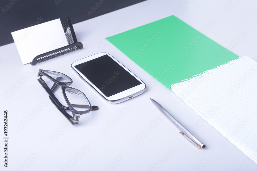 Modern white office desk table with laptop, smartphone and other supplies. Blank notebook page for input the text in the middle. Top view. Modern white office desk table with laptop, smartphone and other supplies. Blank notebook page for input the text in the middle. Top view.