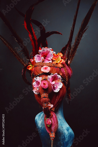 Fototapeta Naklejka Na Ścianę i Meble -  Mannequin in creative headwear with flowers and feathers against dark background