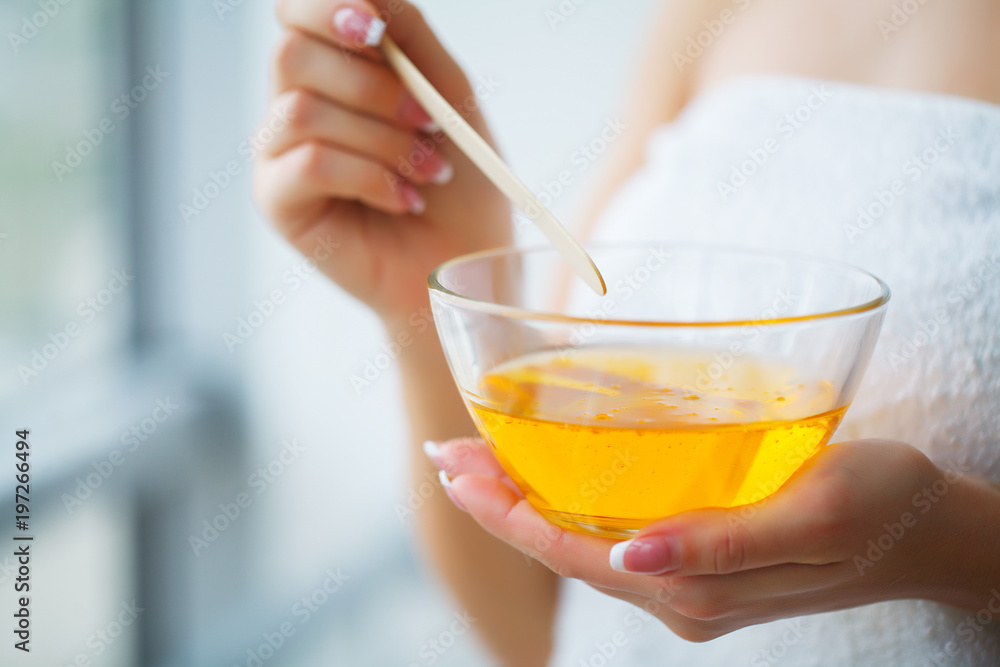 Female hand and orange paraffin wax in bowl. Female hand and orange paraffin wax in bowl.