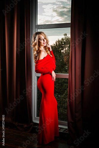 Luxurious woman in red dress posing in the room