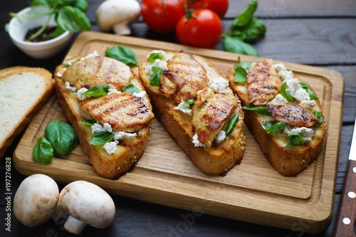 Traditional Italian antipasti bruschetta with grilled chicken, ricotta and basil on wooden board, close up. Appetizing food background