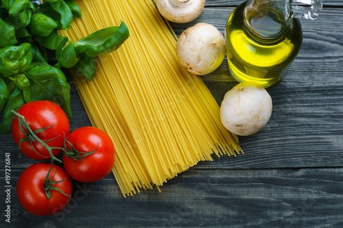 Pasta ingredients. Raw spaghetti, tomatoes, basil, olive oil, mushrooms and spices on wooden table, top view. Italian cuisine food background concept