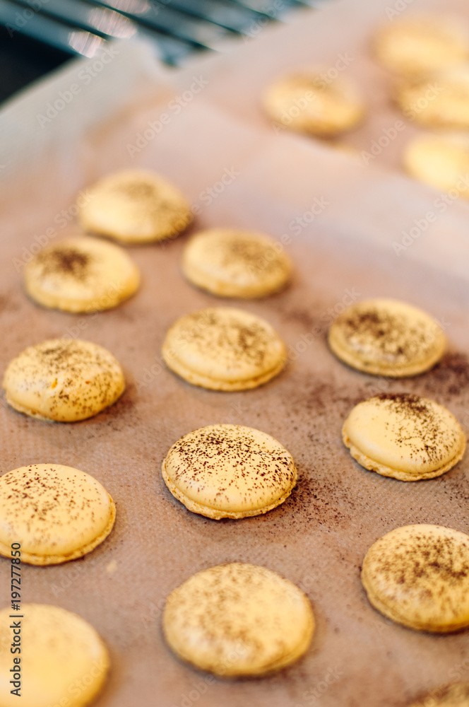 Freshly baked, yellow French Macaron with passion fruit flavor dusted with cocoa powder on silicone mat at baking workshop in France