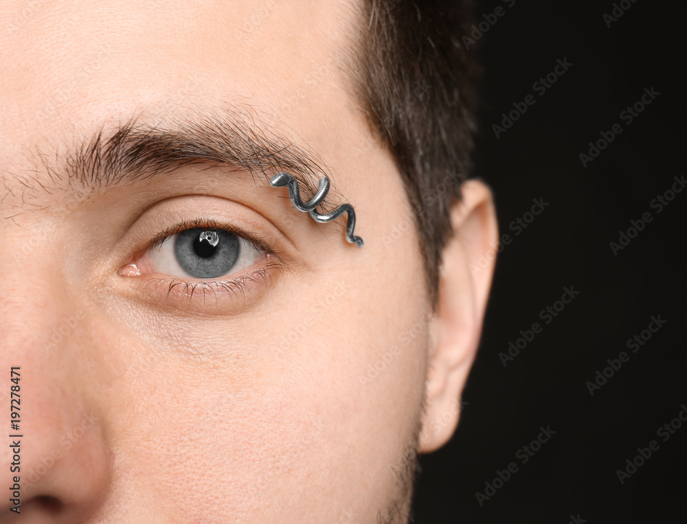 Fototapeta premium Young man with pierced eyebrow on black background, closeup
