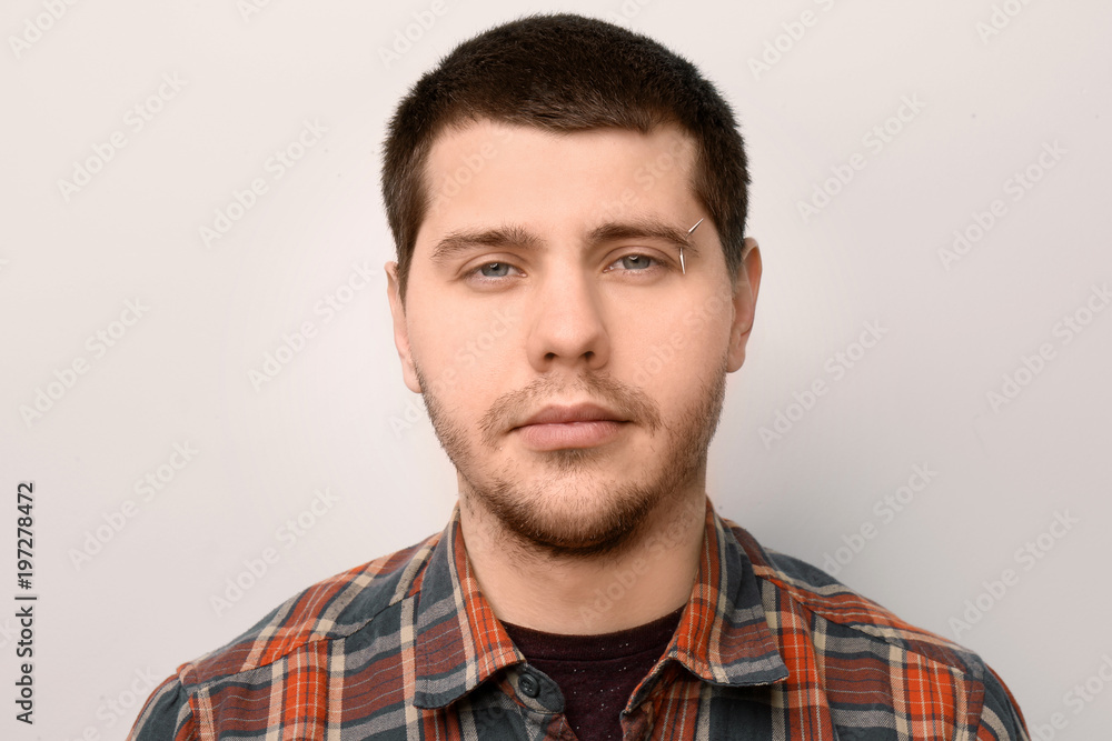 Obraz premium Young man with pierced eyebrow on light background