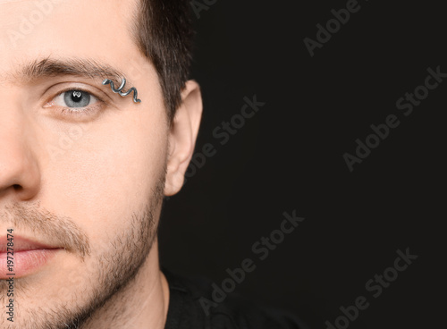 Fotografia Young man with pierced eyebrow on black background, closeup