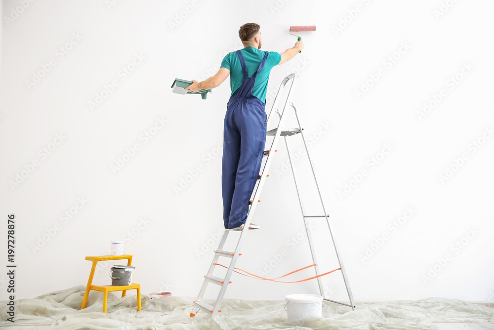 Fototapeta premium Young male decorator painting wall in empty room
