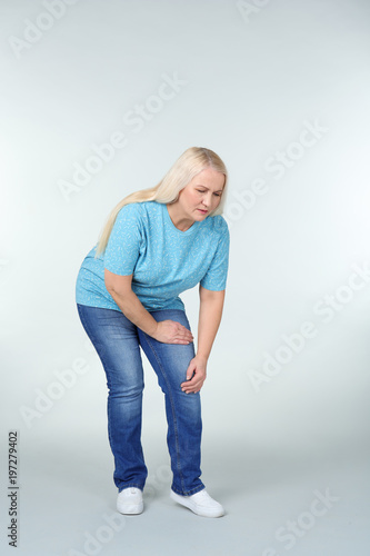 Woman suffering from knee pain on light background