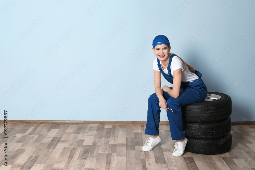 Female mechanic with car tires on grey wall background Female mechanic with car tires on grey wall background