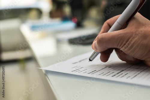 Closeup of hand writing filling job or service application form over light desk background. Signing with pen checklist, college student or education university program certificate. Business contract