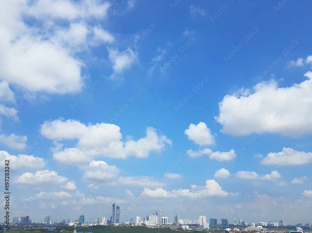 White puffy cumulus clouds computing over cityscape of Johor Bahru, Malaysia with clear blue skies