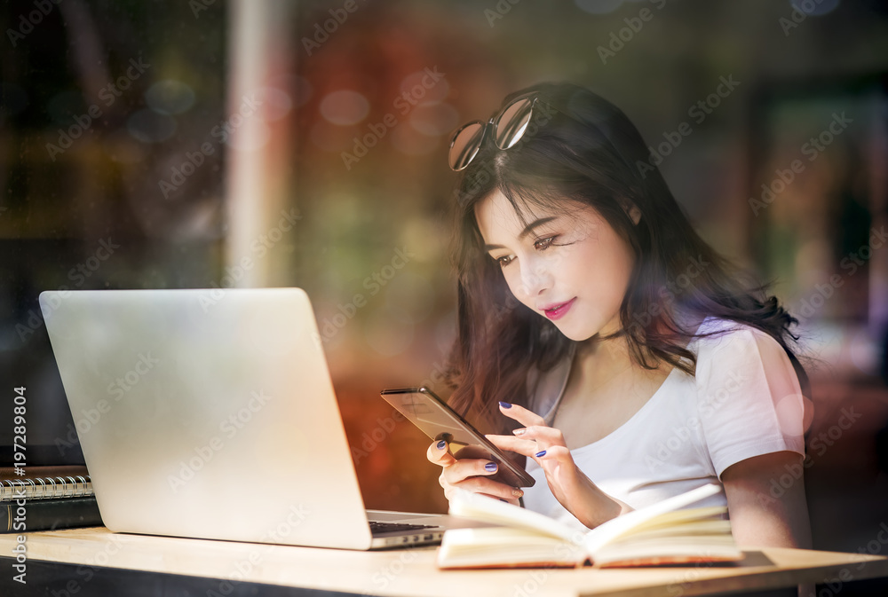 Beautiful white caucasian girl with black hair sitting in cafe and using smartphone while working with laptop. Beautiful white caucasian girl with black hair sitting in cafe and using smartphone while working with laptop.