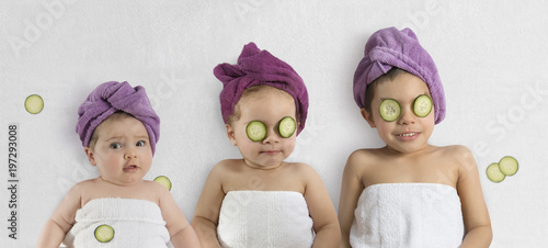 Funny baby girl and kids in white towels and terry cloth bath turbans with cucumber face treatments photo