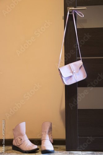 ladies pink handbag hanging on the door, next to the floor are pink boots photo