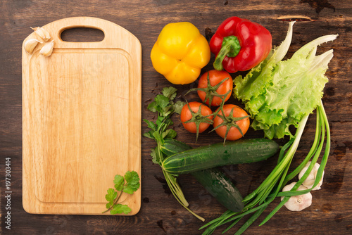 Various vegetables and empty cutting board. Colorful ingredients for cooking on rustic wooden table around empty cutting board with copyspace. Top view.